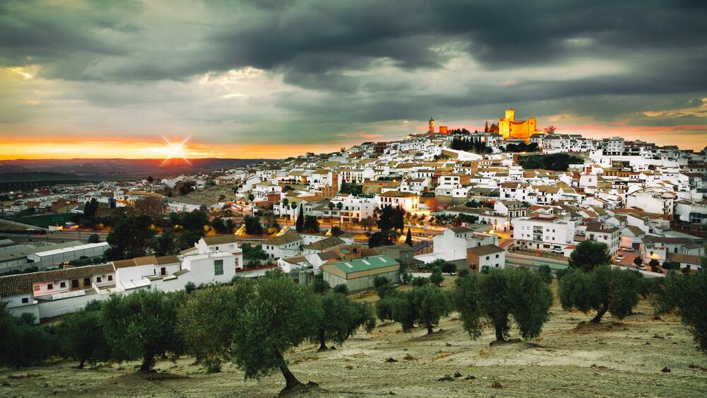 A coastal town with white buildings, a prominent church, and a sunset.