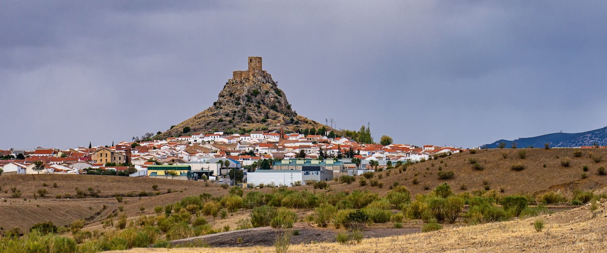 A town with a prominent hilltop fortress and a mountain in the background.
