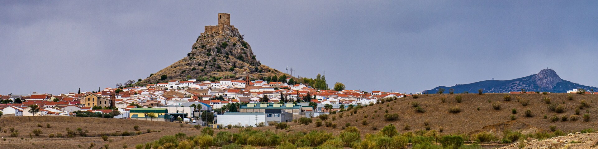 A town with a prominent hilltop fortress and a mountain in the background.
