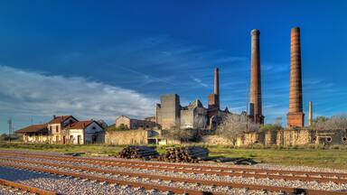A historic industrial complex with tall chimneys, railway tracks, and old buildings.