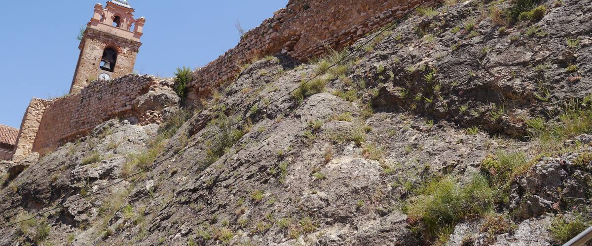 A rocky hillside with a historic stone wall and a bell tower.