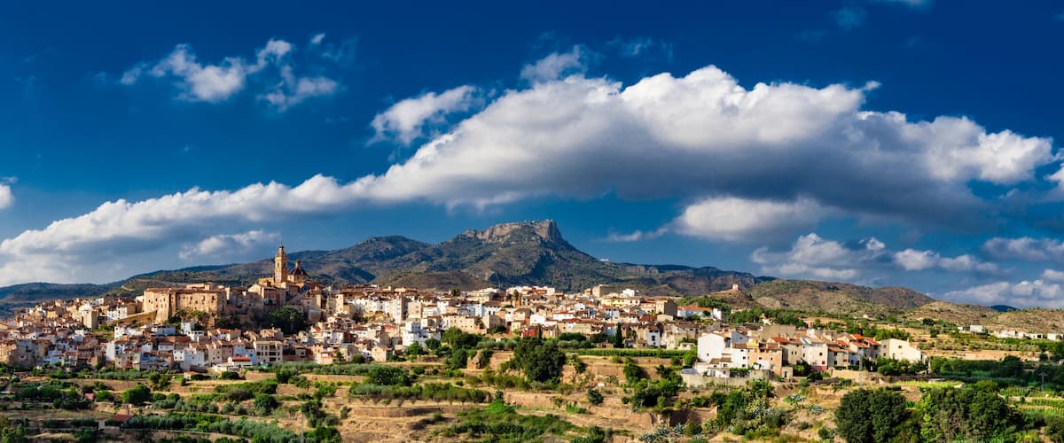 A coastal town with historic architecture, a prominent church, and a mountain range in the background.