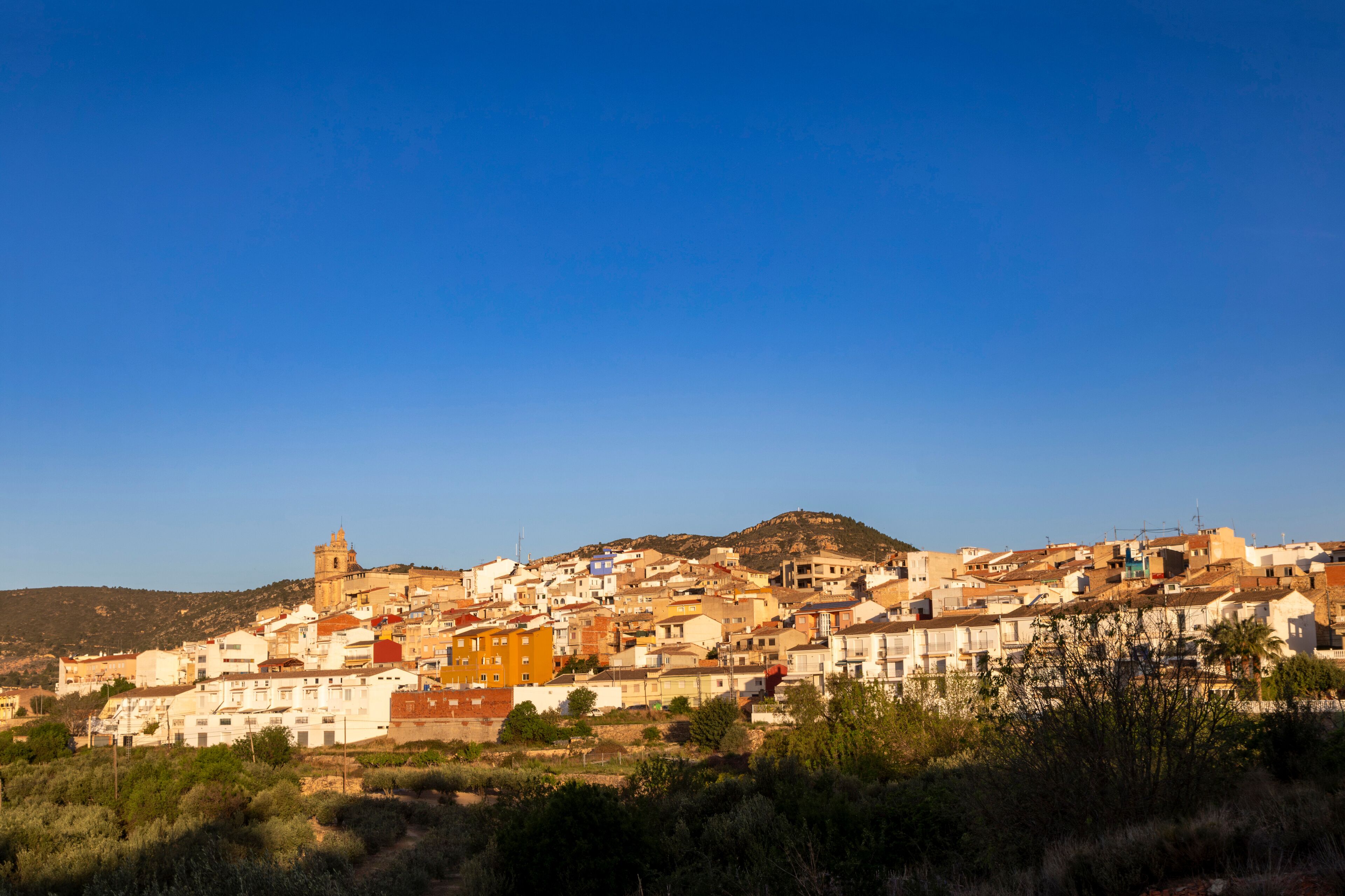 A coastal town with a prominent church on a hill, surrounded by colorful buildings and a clear blue sky.