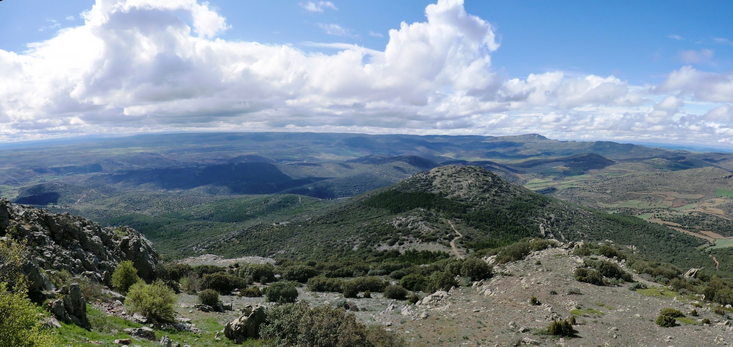 A mountainous landscape with rolling hills, a winding path, and a clear sky with clouds.