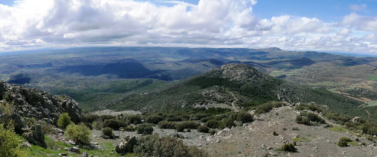 A mountainous landscape with rolling hills, a winding path, and a clear sky with clouds.