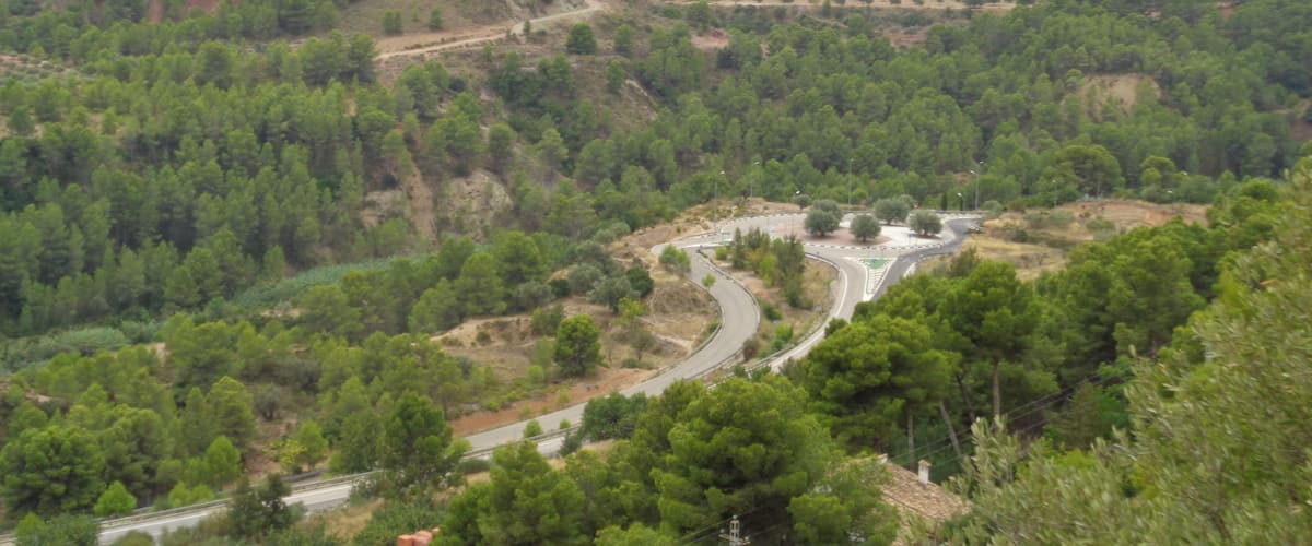 A winding road through a mountainous landscape with dense forests and distant hills.