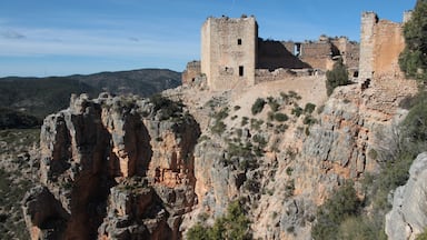 A historic stone castle perched atop a rocky cliff with surrounding mountains.