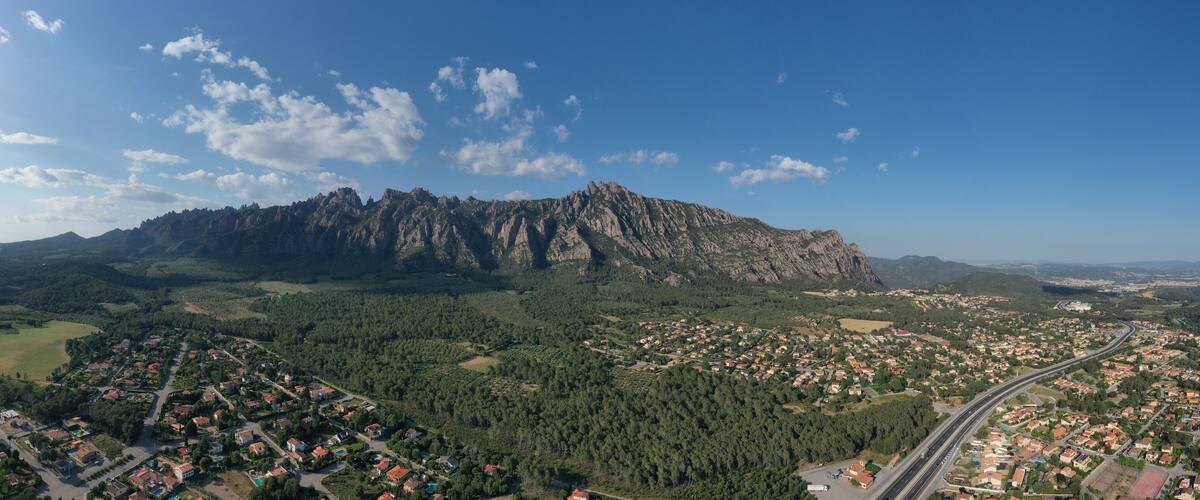 A mountainous landscape with a residential area in the foreground and a dense forest in the background.