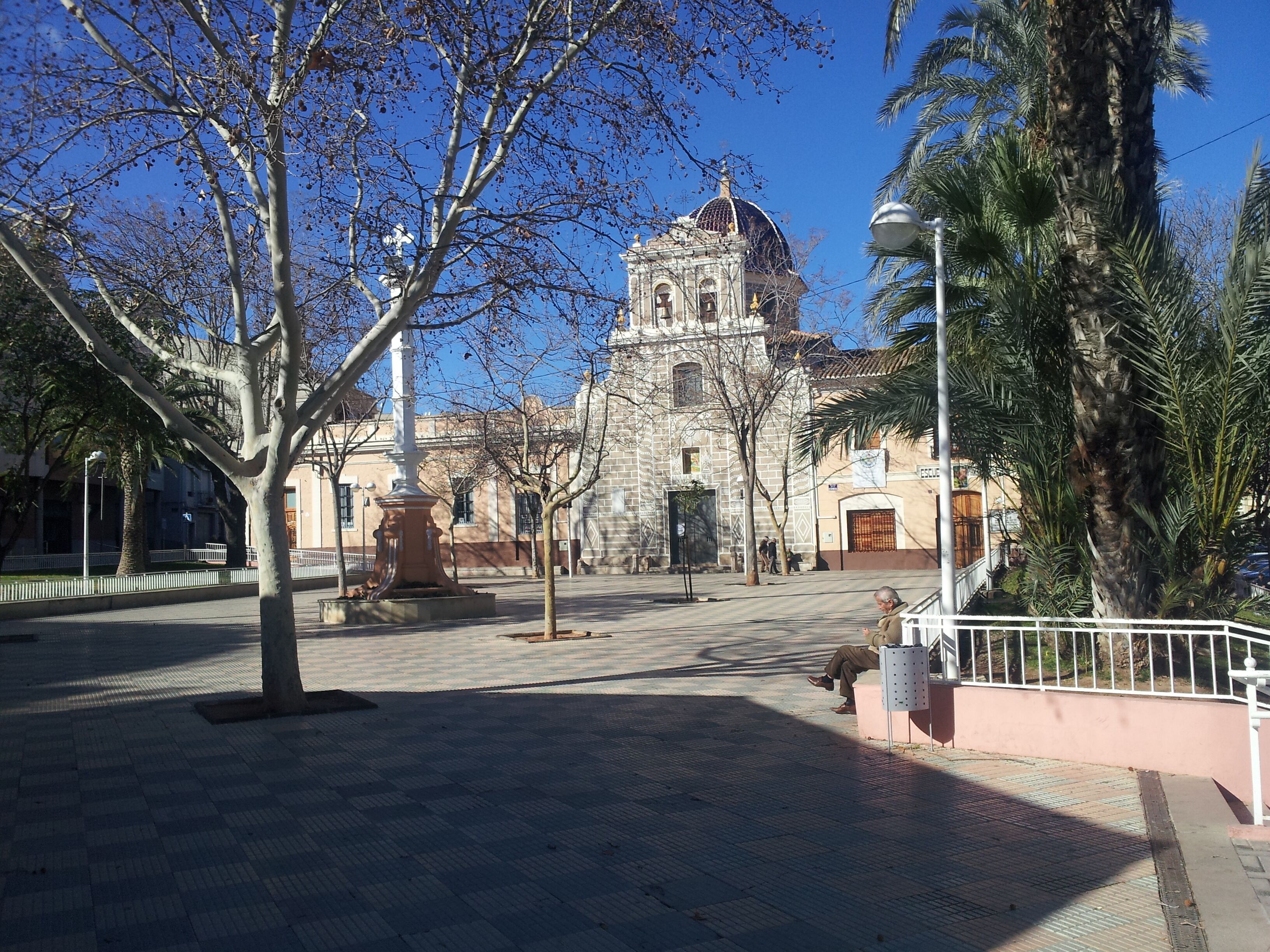 A plaza with a historic building featuring a dome and columns, surrounded by trees and a palm tree.