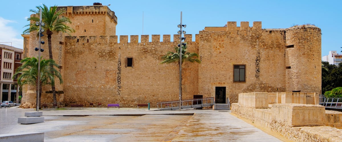 A historic stone fortress with a palm tree in front.