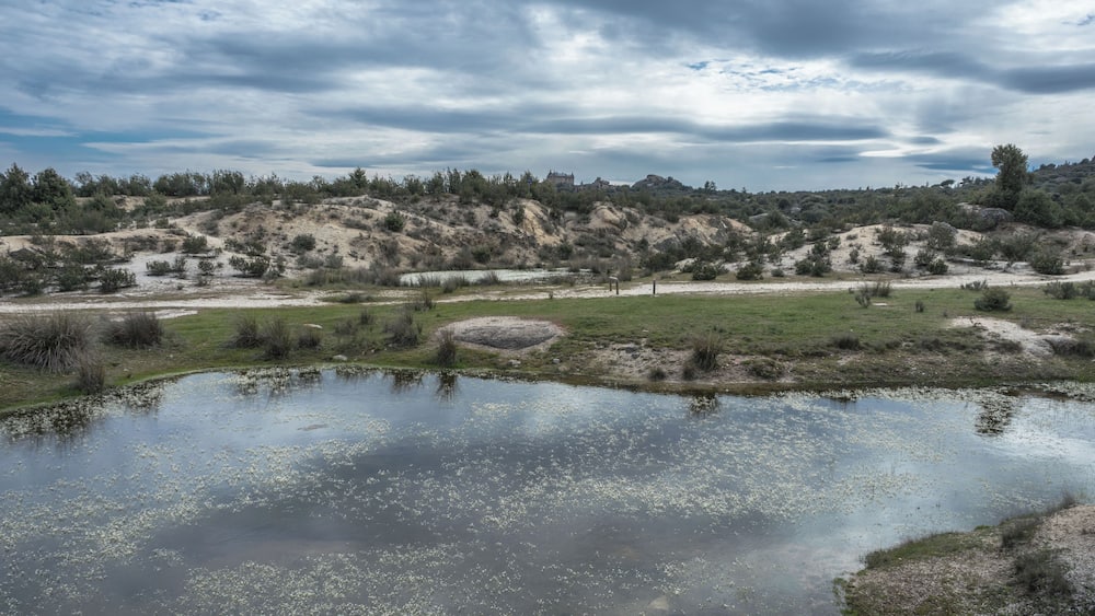 Un paysage comprenant un étang, des zones herbeuses et une colline à la végétation clairsemée.