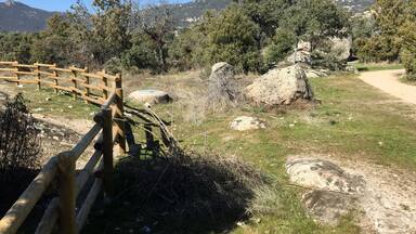 A wooden fence, a dirt path, and a mountainous landscape with trees.