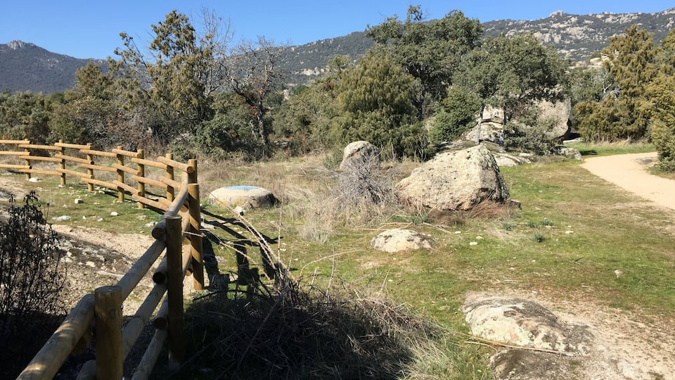 A wooden fence, a dirt path, and a mountainous landscape with trees.