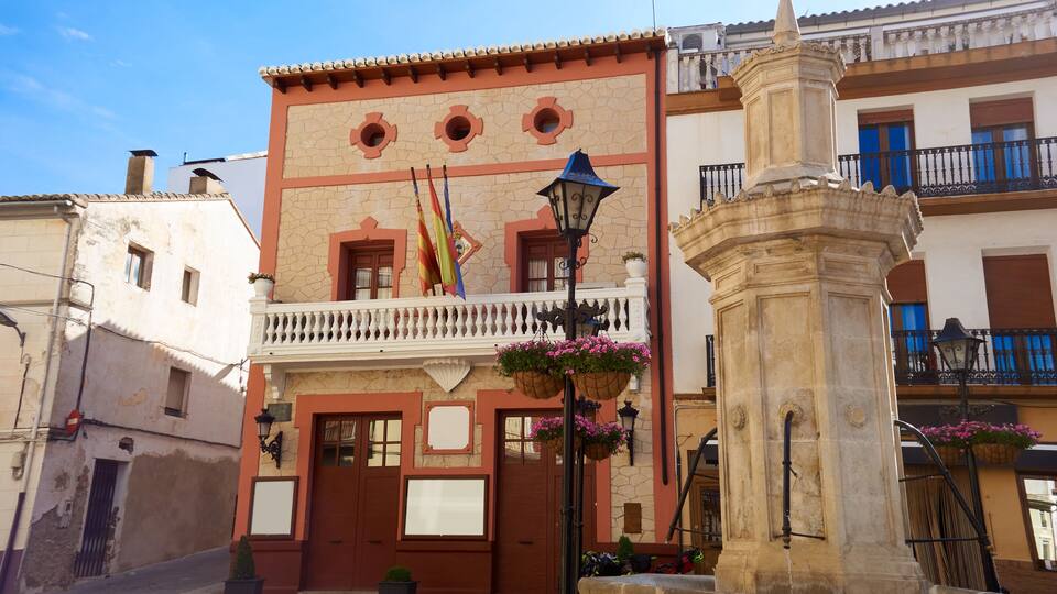 A building with a balcony, a stone fountain, and a flag.