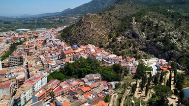 A coastal city with red-roofed buildings, a church, and a hill with a tower.