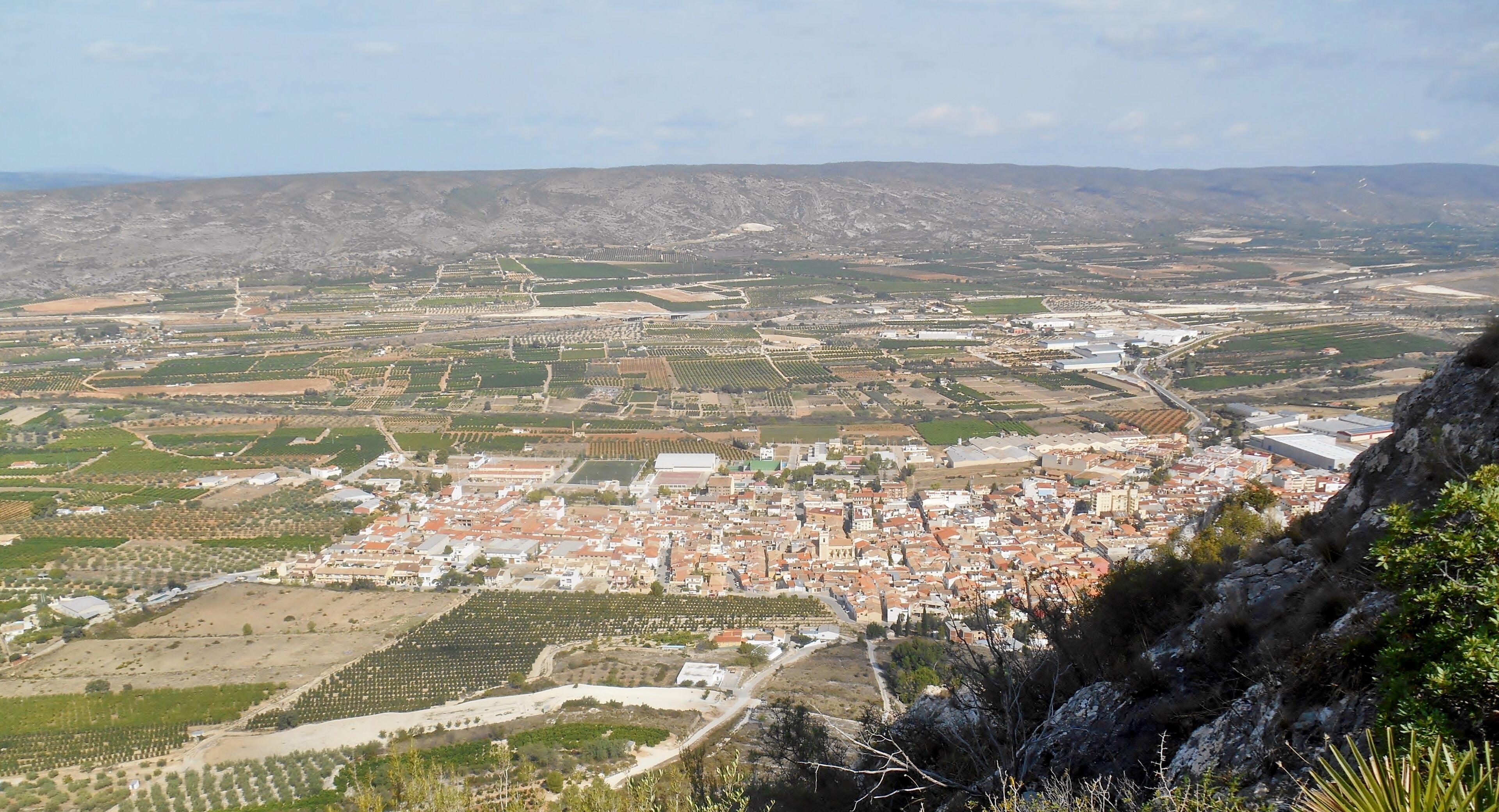 A town with a mix of agricultural fields, residential areas, and a prominent hill in the foreground.