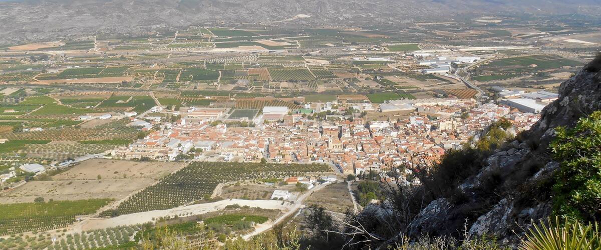 A town with a mix of agricultural fields, residential areas, and a prominent hill in the foreground.