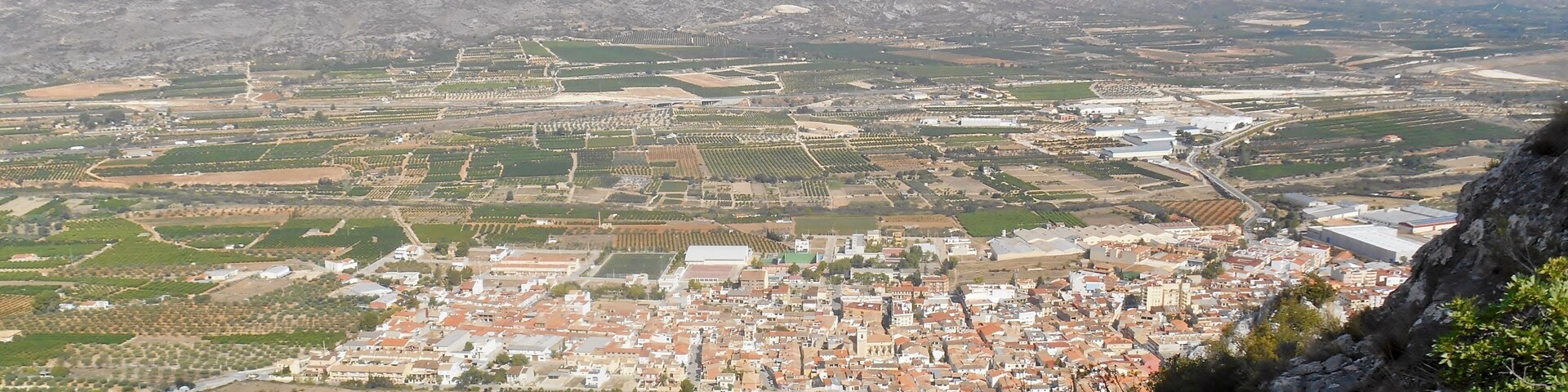 A town with a mix of agricultural fields, residential areas, and a prominent hill in the foreground.