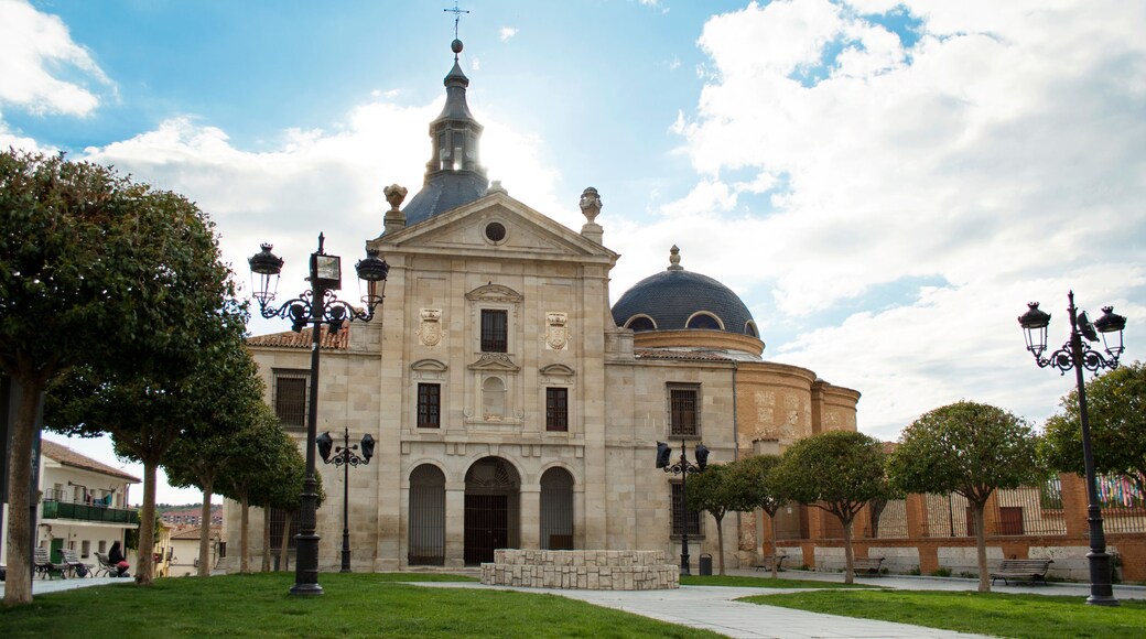 A historic building with a dome and bell tower, surrounded by a park with benches and trees.