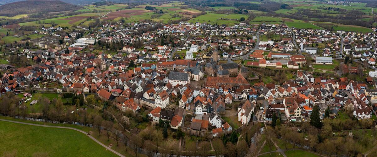 An aerial view of a historic town with a prominent church, surrounded by rolling hills and green fields.