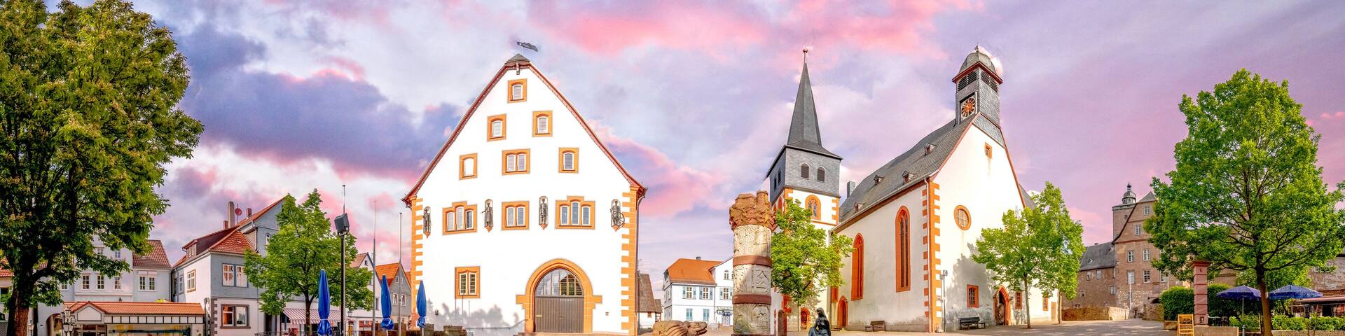 A cobblestone square with historic buildings, a church, and a statue in the center.