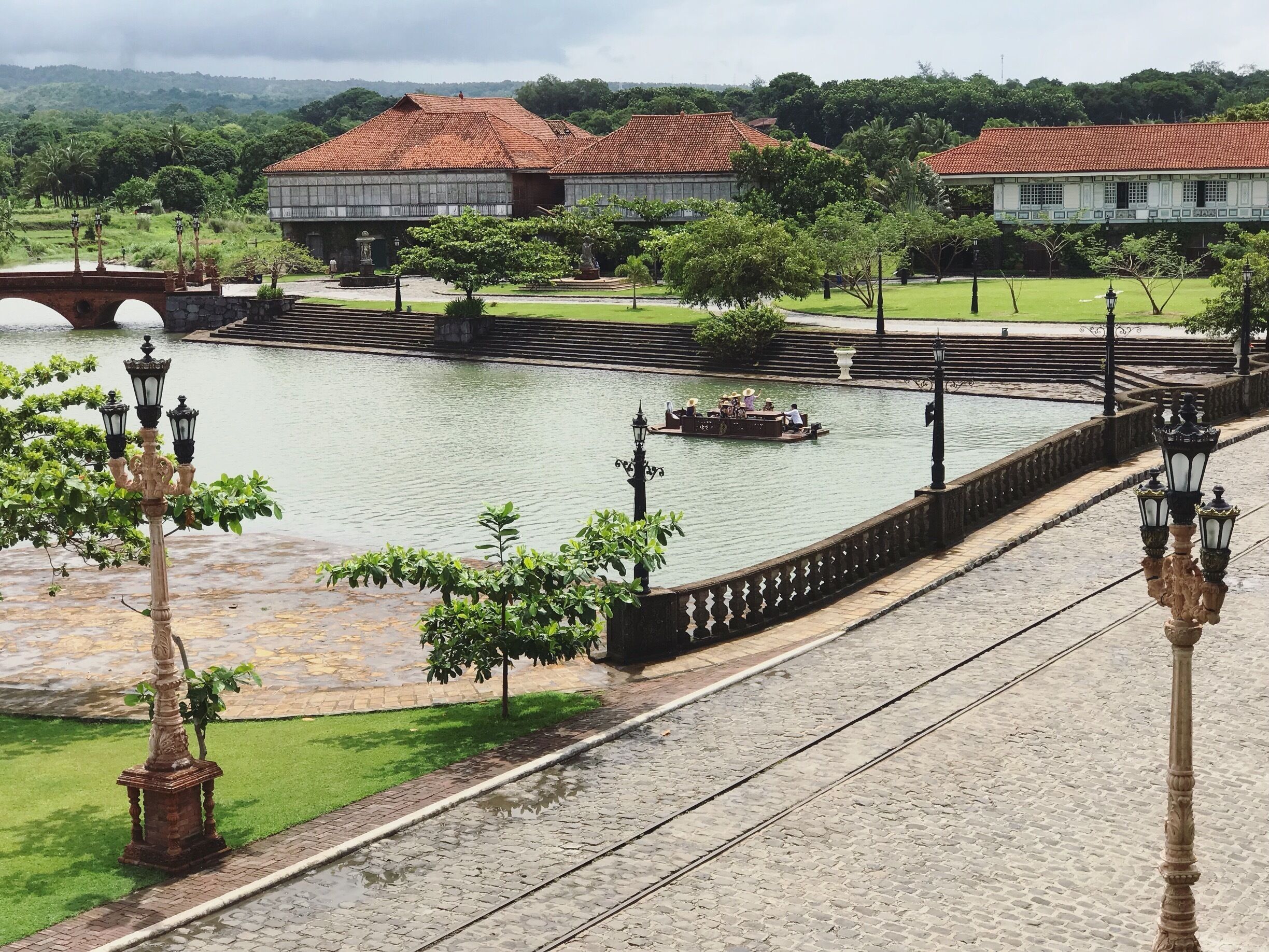 Un paseo fluvial con un puente, edificios y una barca con gente.