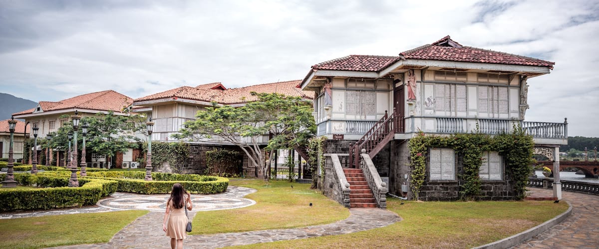 A traditional courtyard with stone pathways, a woman walking, and buildings with tiled roofs.
