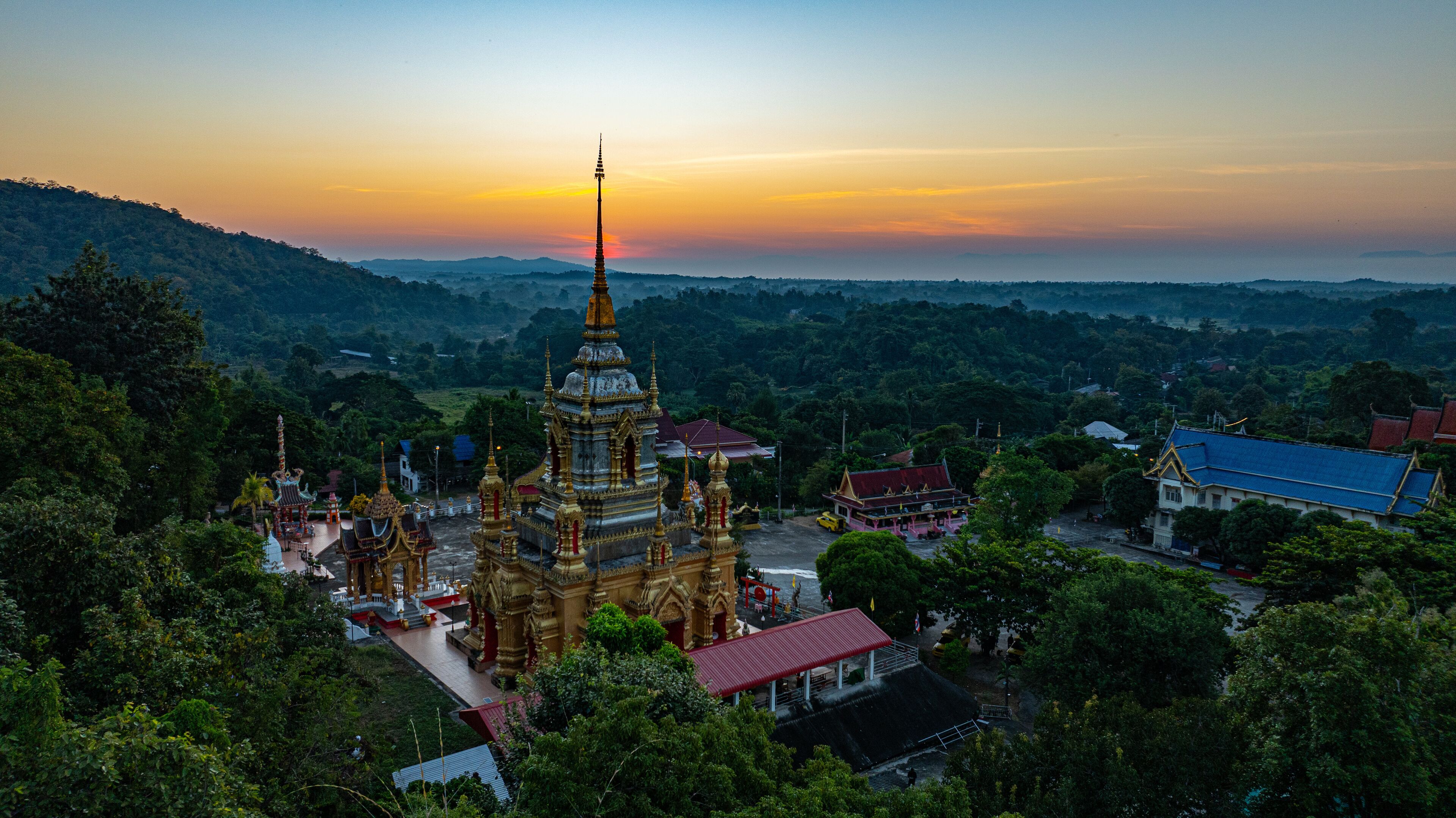 Aerial view of Mae Klang Waterfall Temple in Chiang Mai with the sunrise casting warm hues in calm sky. The tranquil setting highlights the serene beauty of the temple and the natural landscape.