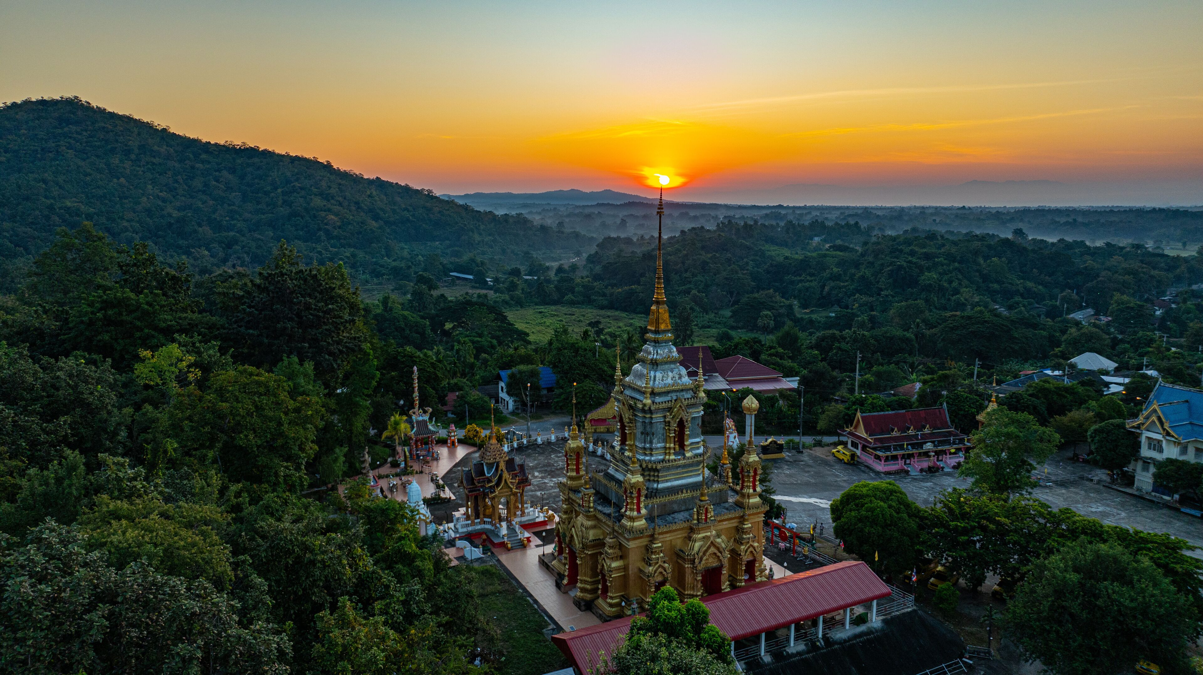 Aerial view of Mae Klang Waterfall Temple in Chiang Mai with the sunrise casting warm hues in calm sky. The tranquil setting highlights the serene beauty of the temple and the natural landscape.