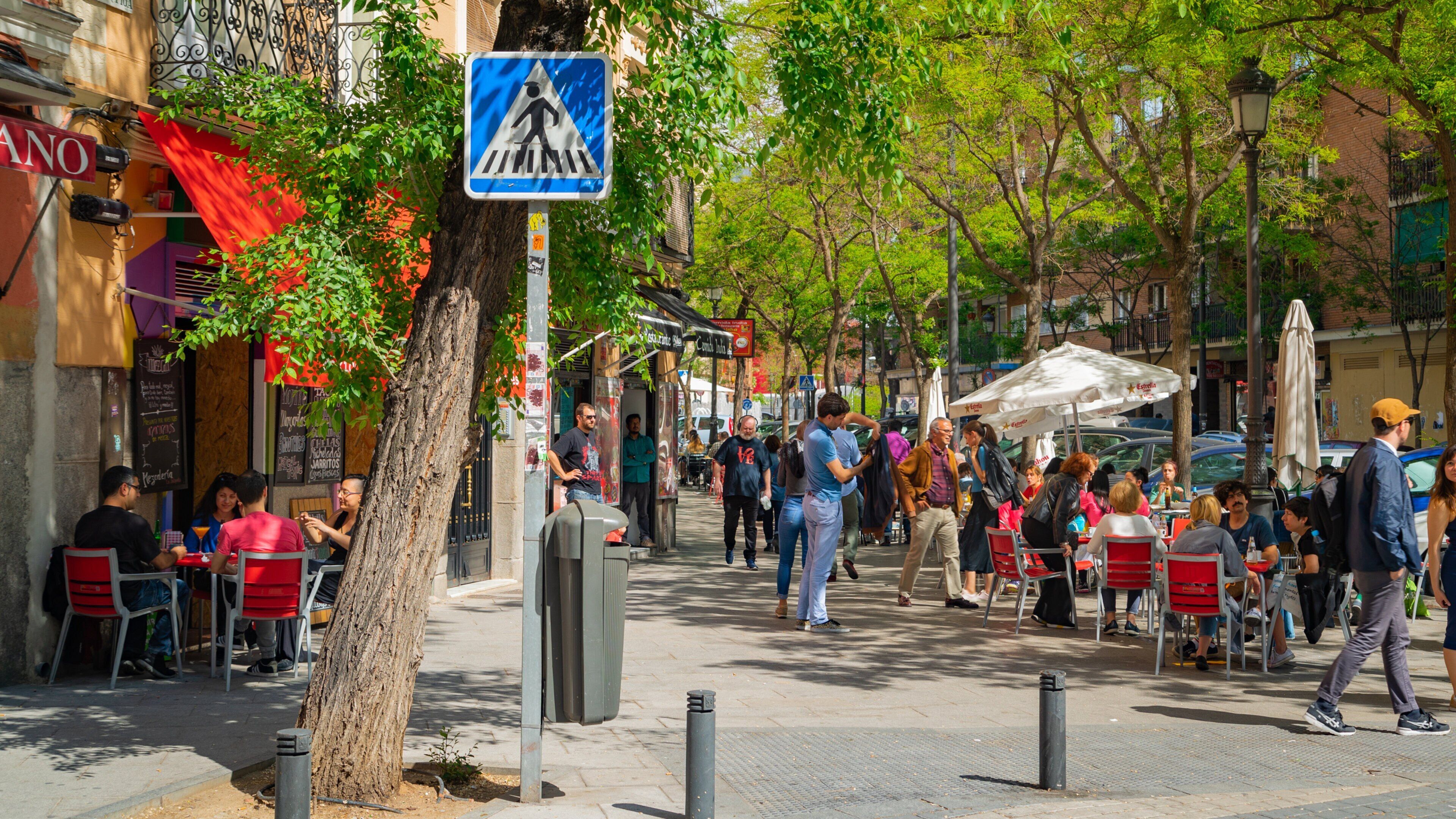 Una calle concurrida con peatones, cafés al aire libre y una señal de paso de peatones.