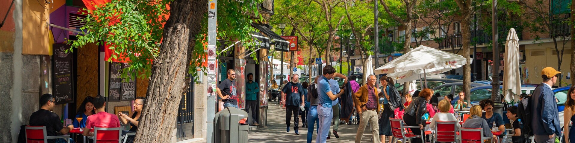 Una calle concurrida con peatones, cafés al aire libre y una señal de paso de peatones.