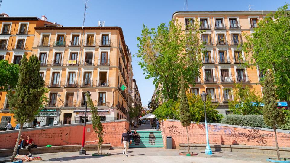 A street with buildings, trees, and a brick wall with graffiti.