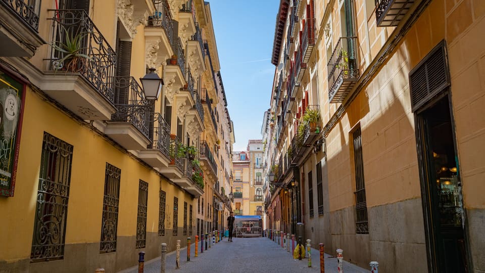 A narrow cobblestone street flanked by yellow buildings with ornate balconies and wrought iron railings.