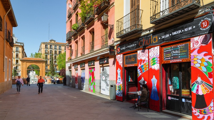 A street with colorful storefronts, including one with a mural of a woman and a dress.