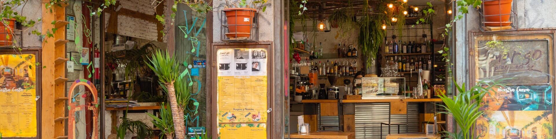 A rustic storefront with wooden shutters, potted plants, and a menu board.