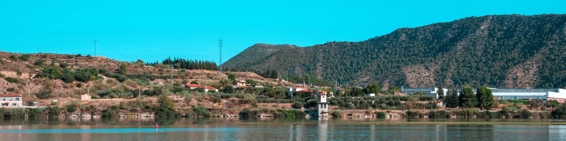 Un lago tranquilo con aguas azul cristalino, rodeado de colinas y vegetación escasa.
