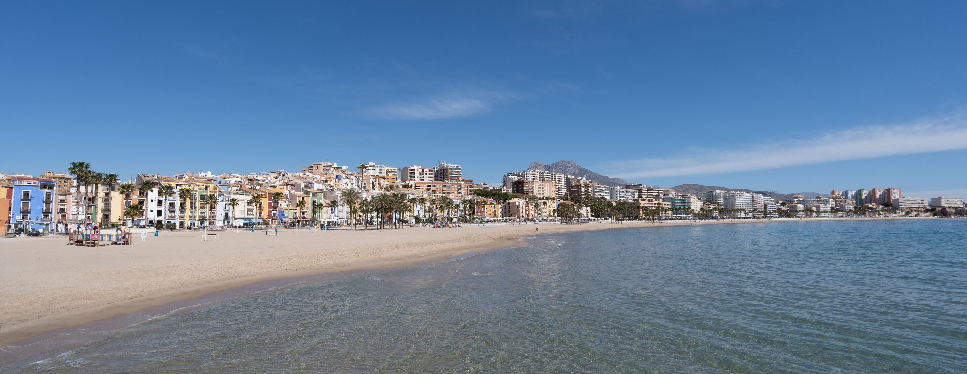 A coastal cityscape with a sandy beach, colorful buildings, and a mountain in the background.