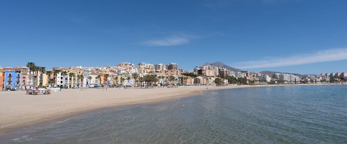 A coastal cityscape with a sandy beach, colorful buildings, and a mountain in the background.