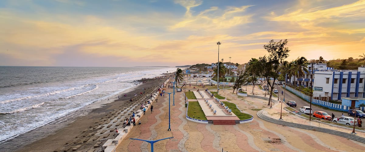 A beach with a promenade, palm trees, and buildings in the background.