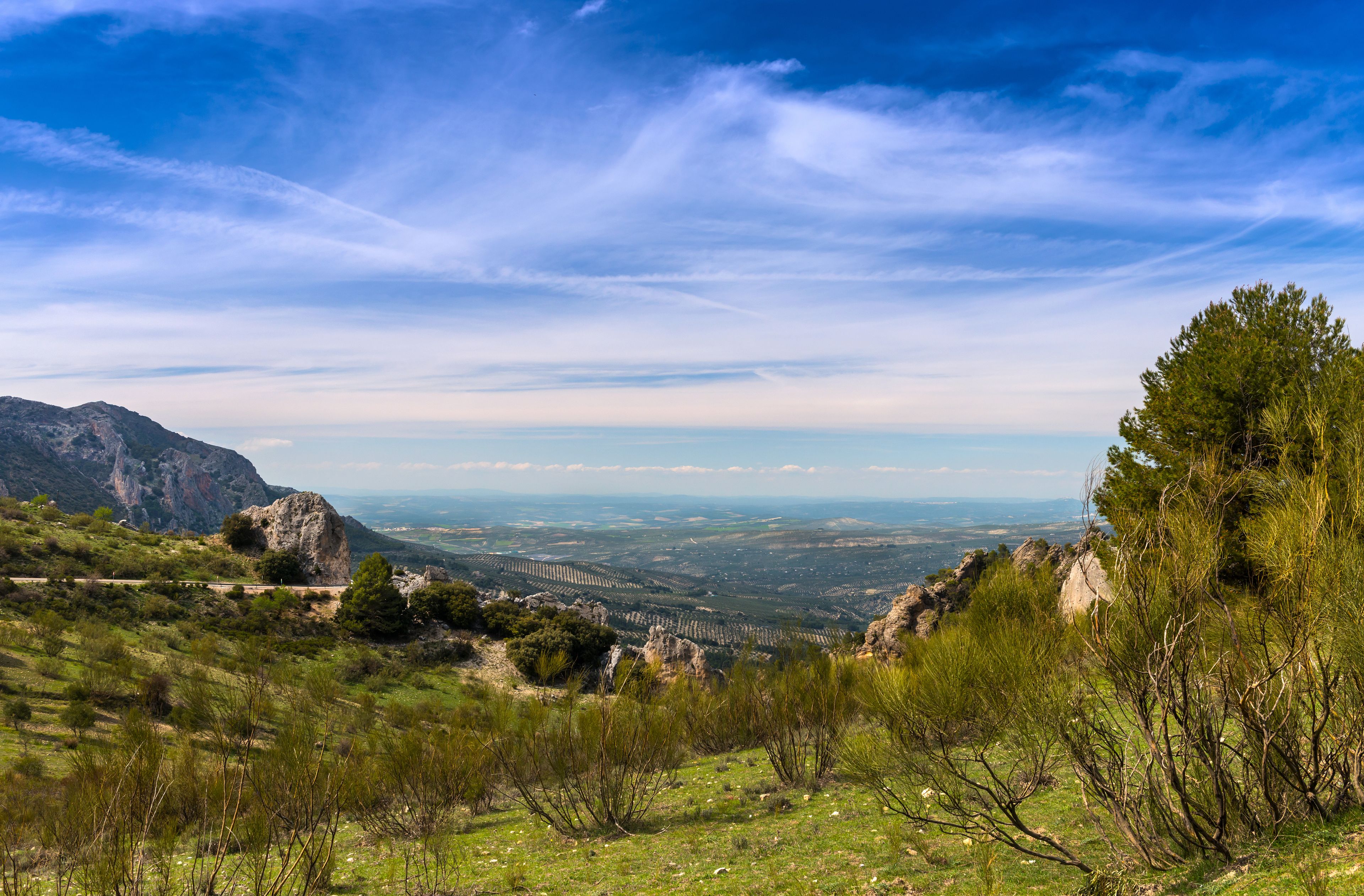 A mountainous landscape with a clear sky, a road, and distant fields.