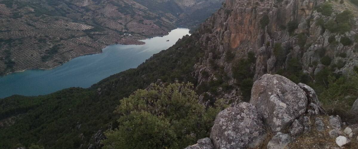 A mountainous landscape with a lake surrounded by rocky terrain and sparse vegetation.