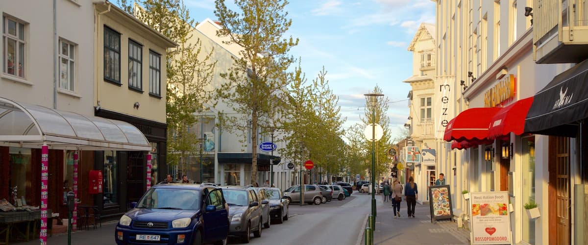 A street lined with parked cars, storefronts, and pedestrians.