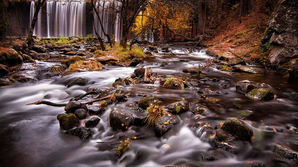 Arroyo de montaña con cascada bañado de hojas secas del otoño en Rascafría Madrid