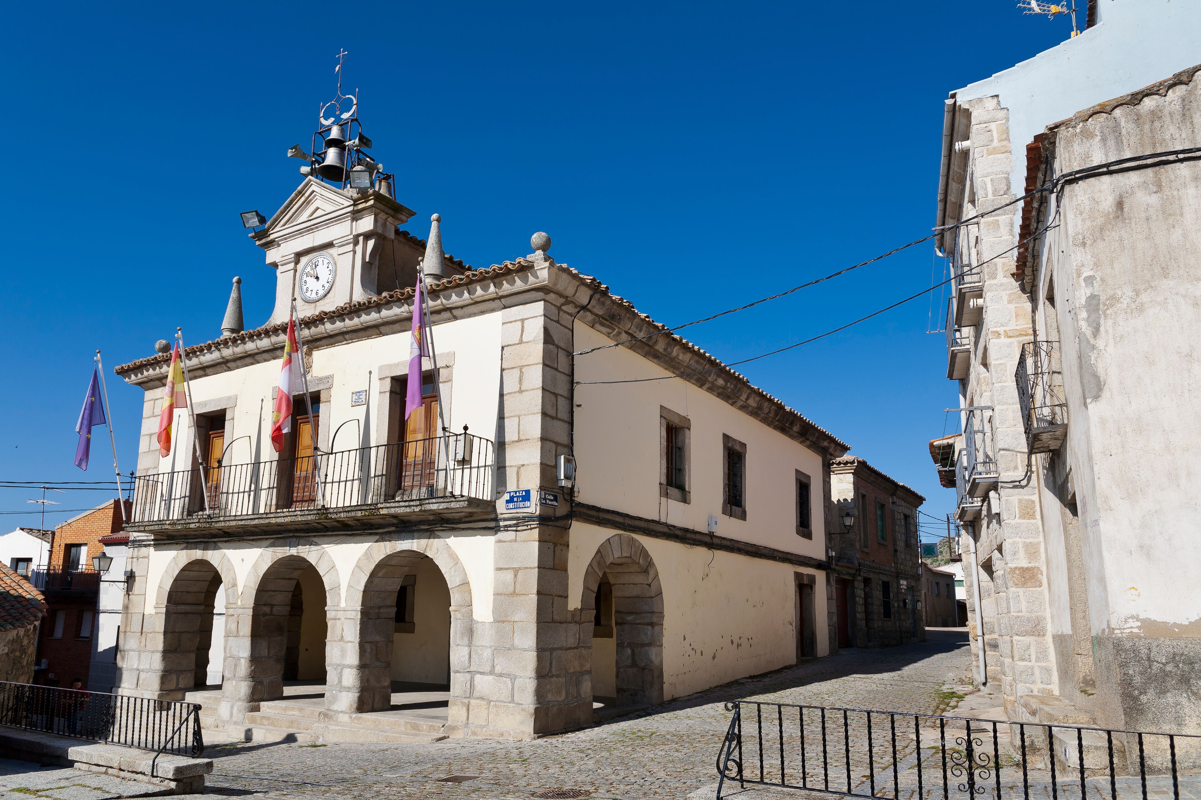 A historic building with a clock tower, arched windows, and flags.