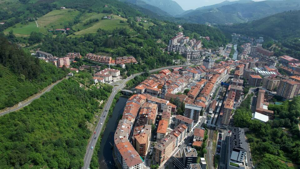 An aerial view of a town with a river running through it, surrounded by green hills.