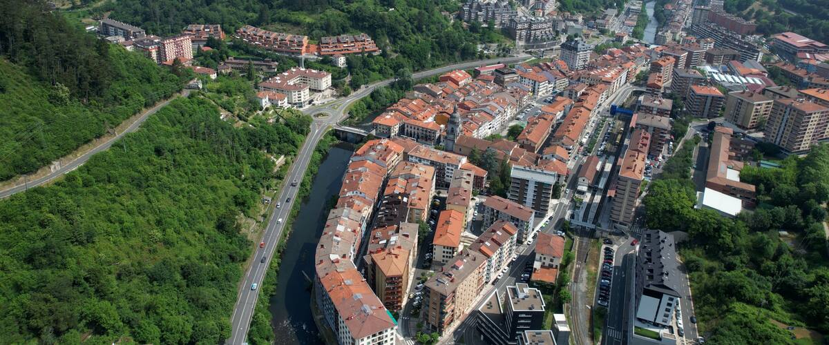 An aerial view of a town with a river running through it, surrounded by green hills.