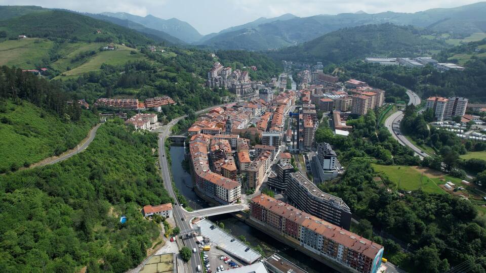 A city with a river running through it, surrounded by green hills and mountains.