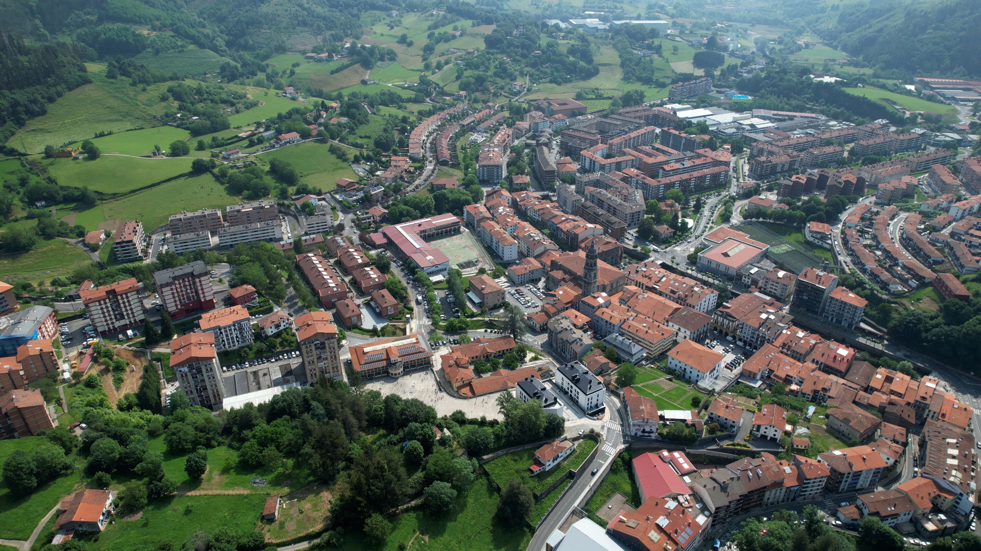 An aerial view of a town with dense residential buildings, green fields, and a central open space.