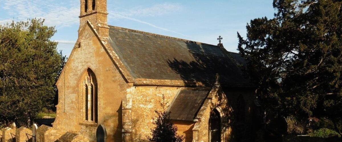 A historic stone church with a bell tower, arched windows, and a grassy courtyard.