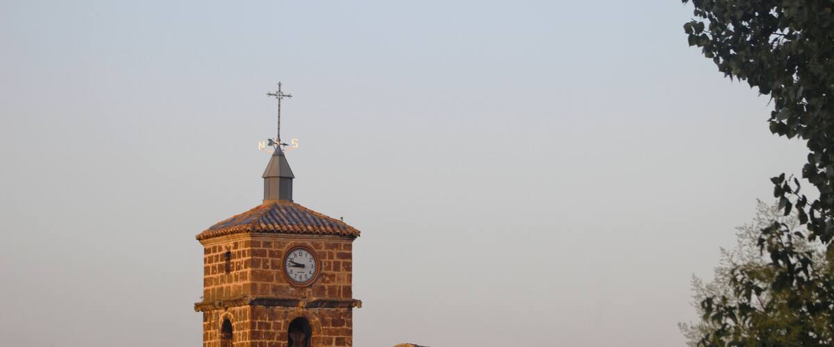 A historic stone tower with a clock, surrounded by traditional buildings with tiled roofs.